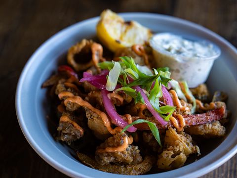 Crispy calamari topped with pickled red onion and green onion, with a lemon wedge and tzatziki