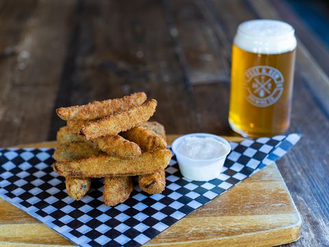 Battered pickle spears with ranch, next to a pint in a Post & Row Brewing Co. glass