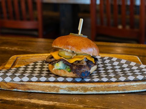 A smash burger with melted cheddar, pickles, onions and lettuce on a toasted brioche bun, served on checkered paper on a wooden board
