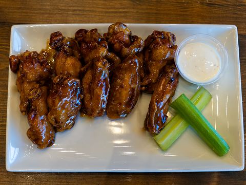 A plate of saucy chicken wings with ranch and celery sticks