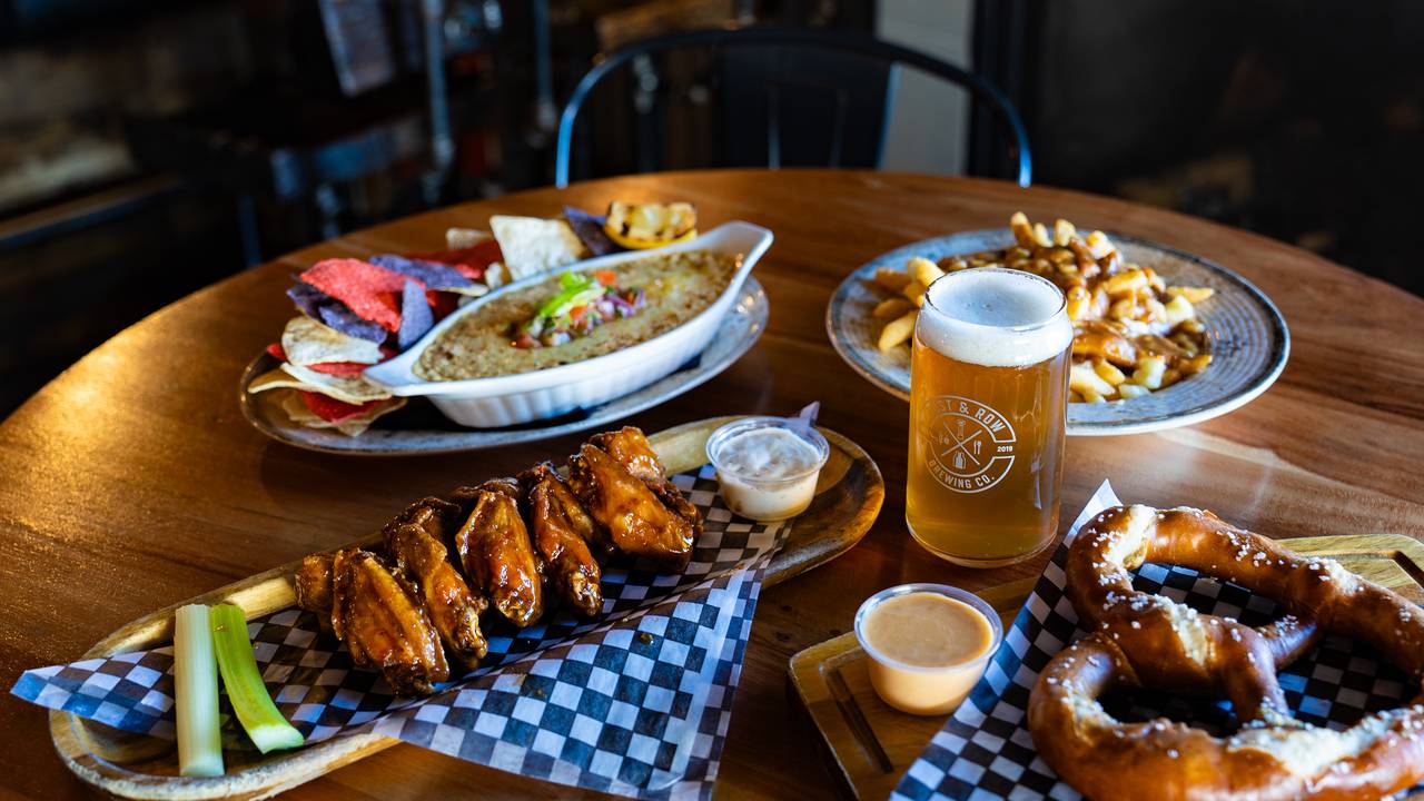 Chicken wings, a soft pretzel with beer cheese, poutine and tortilla chips with dip around a pint in a Post & Row Brewing Co. glass