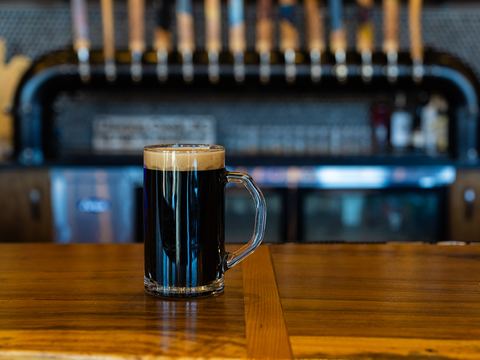 A mug of dark beer with a creamy head on the wooden bar, in front of our row of tap handles