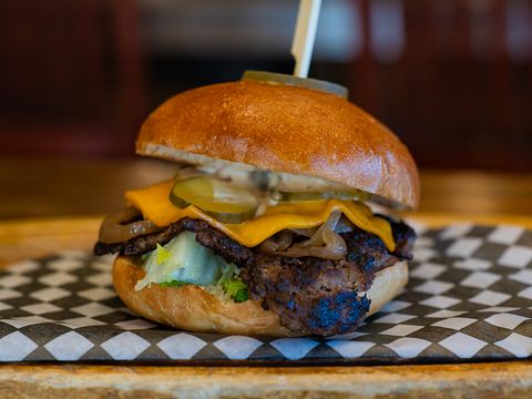 Close-up of a smash burger: a crispy-edged beef patty, melted cheddar, pickles, onions and lettuce on a toasted brioche bun
