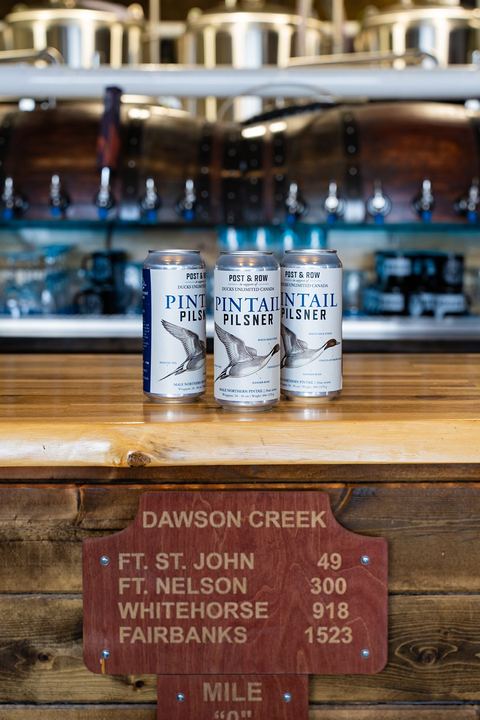 Three cans of Pintail Pilsner on our bar above the Dawson Creek Mile 0 signpost