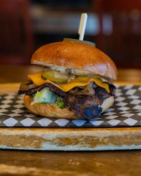 A smash burger with melted cheddar, pickles and onions on a toasted brioche bun